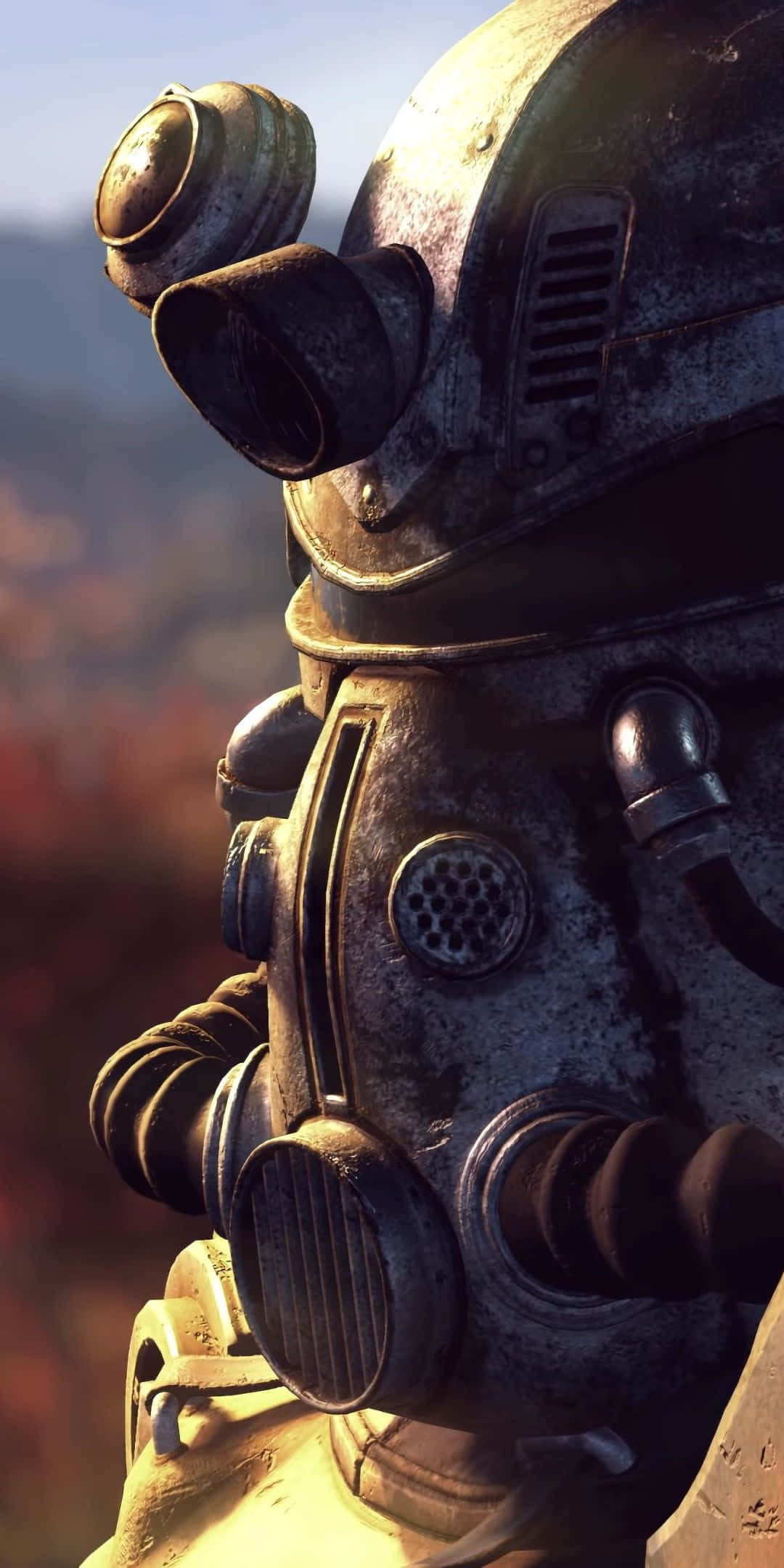 用 Pixel 3 和 Fallout 76 解開廢土的奧秘 壁紙 — 特寫一個風化的金屬動力裝甲頭盔，帶有發光面罩，背景是朦朧的秋日景色。