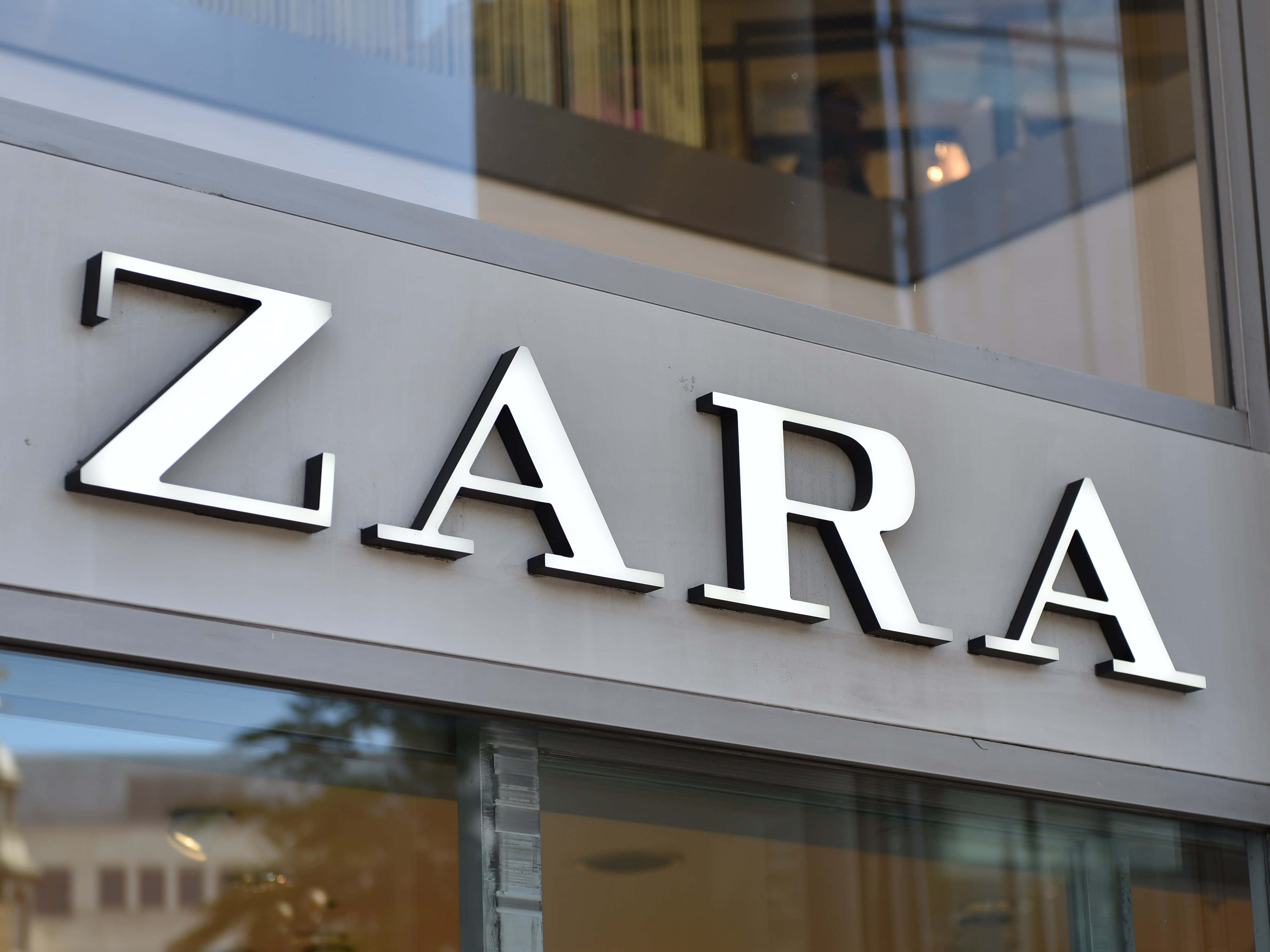 用 Zara 提升你的造型 壁紙 — 現代玻璃幕牆建築外牆上安裝的時尚銀色ZARA商店標誌特寫。