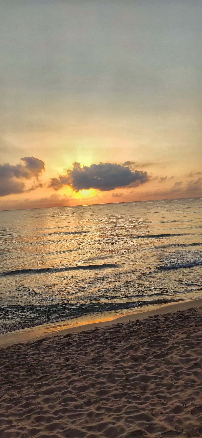 海洋上的日落，金色光芒和烏雲在沙灘上方。