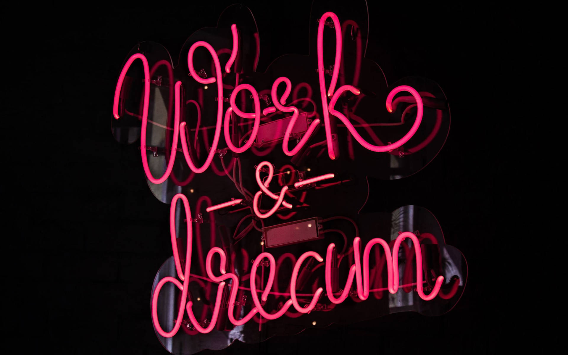 深色磚牆上寫著「Work & Dream」的粉紅色霓虹燈牌。