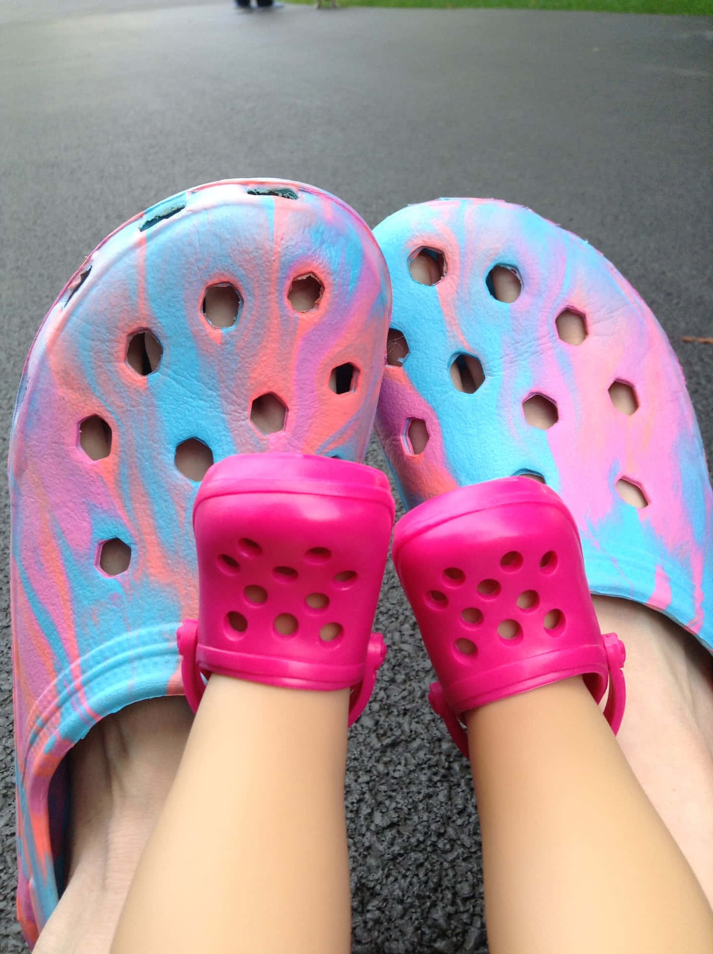 腳穿彩色紮染Crocs涼鞋在人行道上。