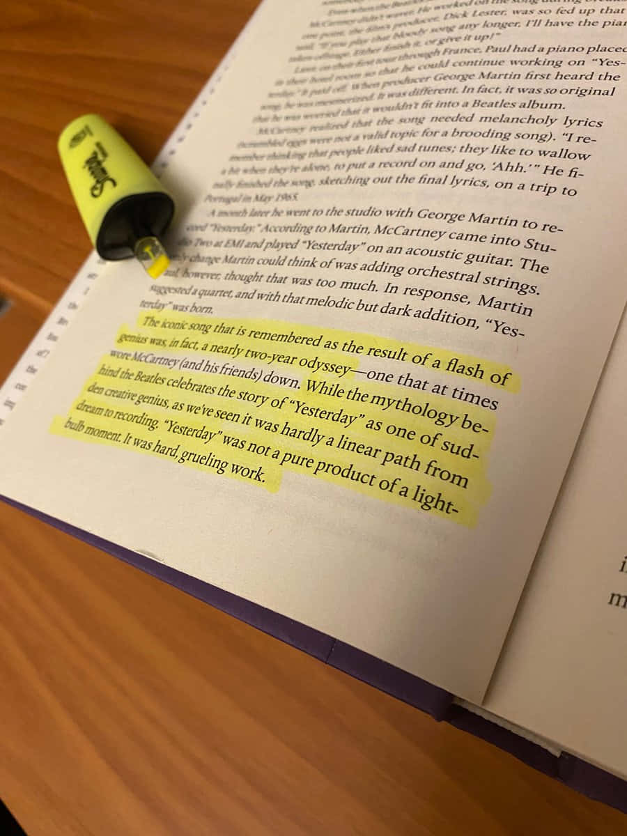 用Highlight為你的日子增添亮色 壁紙 — 一本打開的書的特寫，書頁上有黃色螢光筆標記，並有一支綠色螢光筆擱在頁面上。