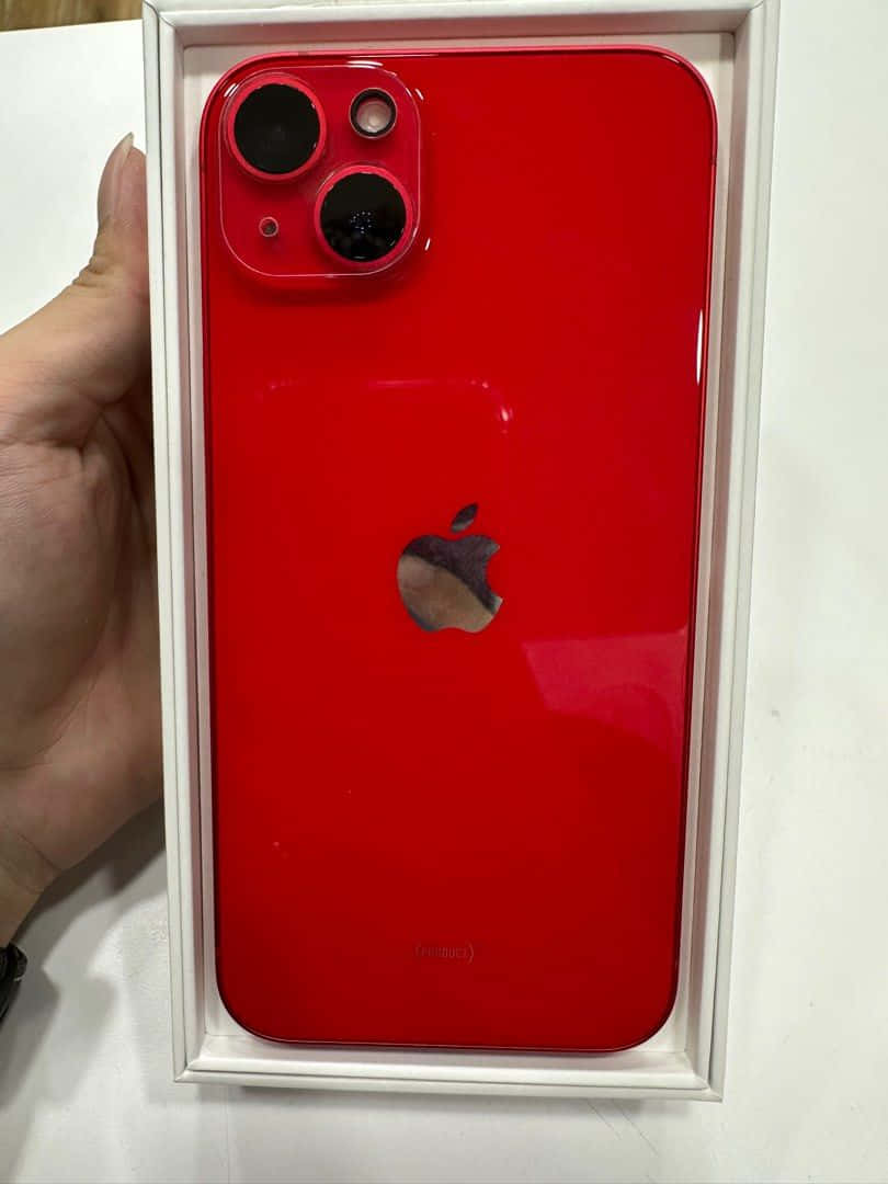 用iPhone享受生活的小確幸 壁紙 — 一隻手拿著白色盒子裡的鮮紅色 iPhone 13 mini，展示其光亮的背面和相機模組。