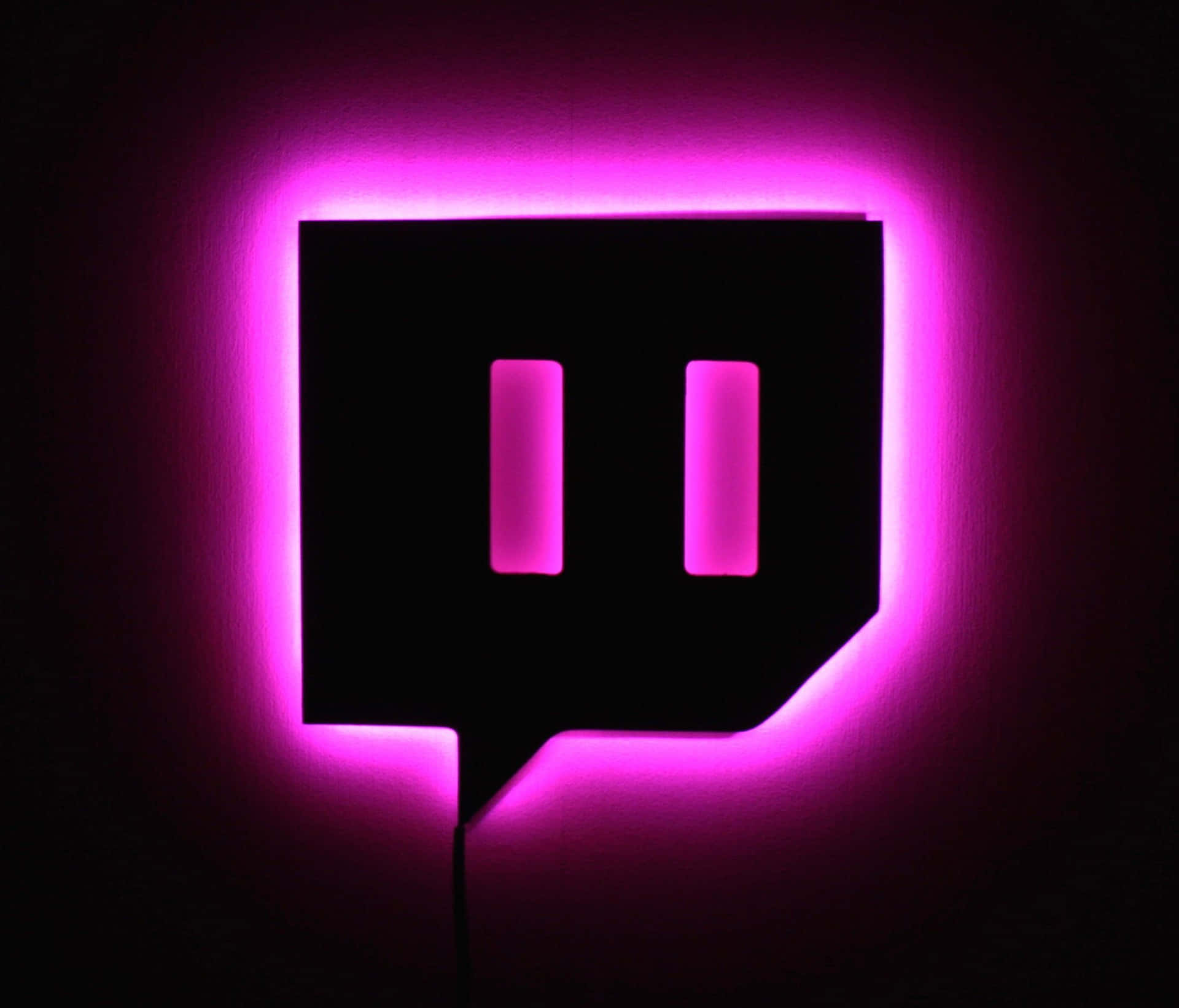 一個發光的粉紅色Twitch標誌招牌在黑暗的牆壁上。