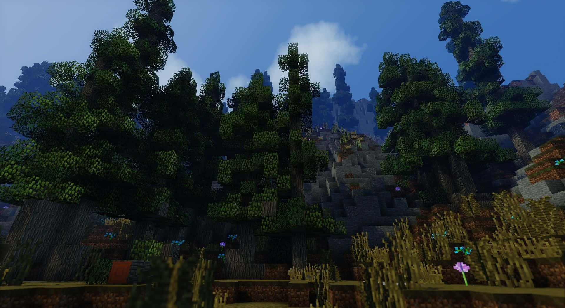 用Shaders打造屬於你的Minecraft之路 壁紙 — 一個像素化的Minecraft森林，有高聳的樹木和岩石丘陵，在晴朗的藍天下有蓬鬆的雲朵。