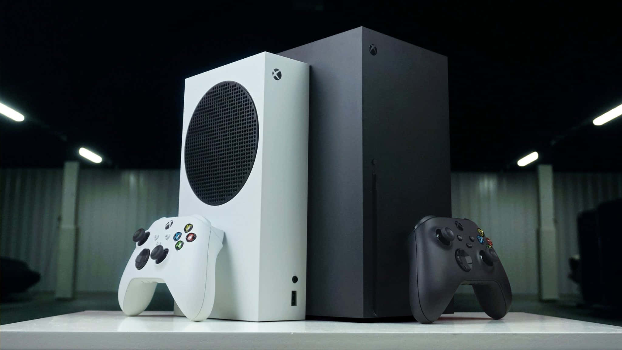 兩部 Xbox 主機連手掣放在白色桌子上，在攝影燈光下。
