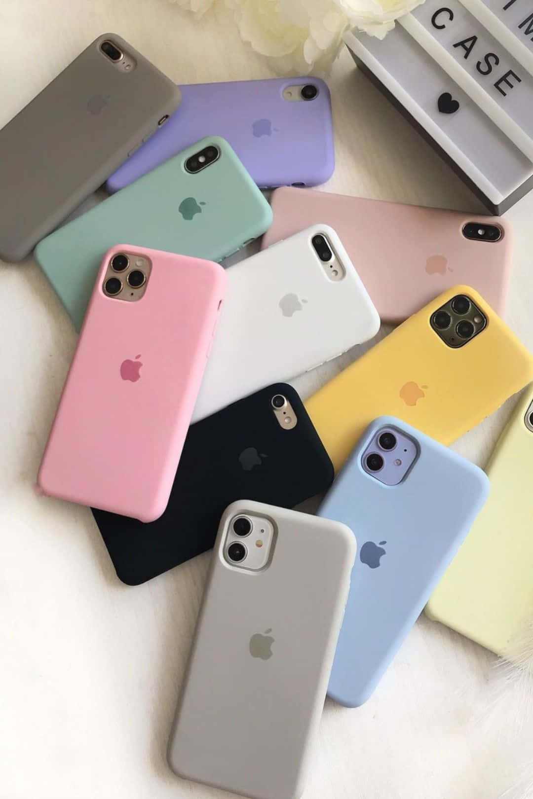 用全新 Apple iPhone 12 捕捉世界之美 壁紙 — 一系列色彩繽紛的Apple iPhone保護殼，以柔和白色表面搭配花卉裝飾，呈現粉彩和純色調。