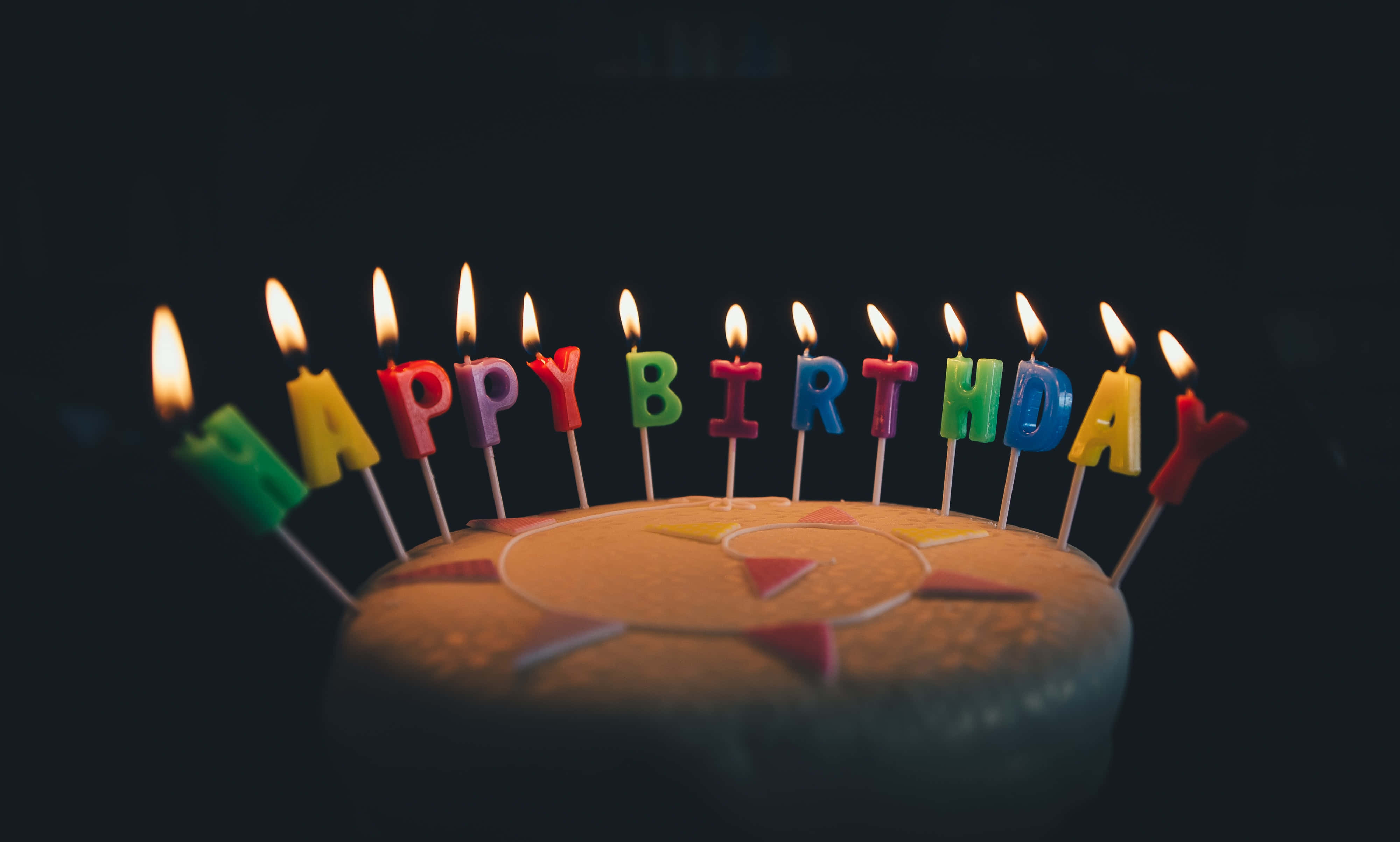 用可愛生日慶祝吧！ 壁紙 — 一個生日蛋糕，上面有彩色字母蠟燭拼出「生日快樂」，在黑暗背景中閃耀。