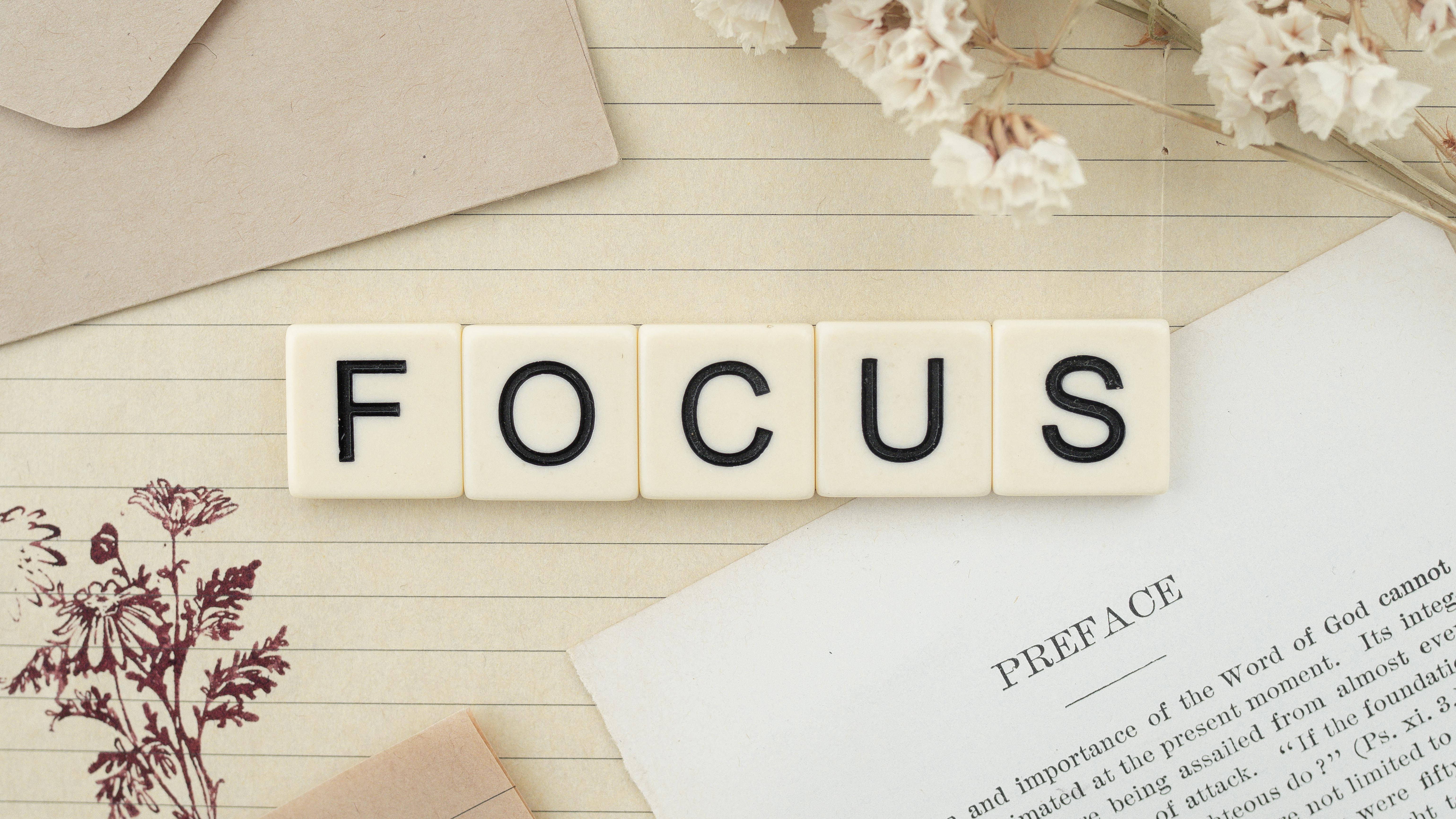 鼓舞人心的 桌布 壁紙 — 用奶油色瓷磚拼出的單詞FOCUS放在橫線紙上，旁邊有乾花和一本打開的書。