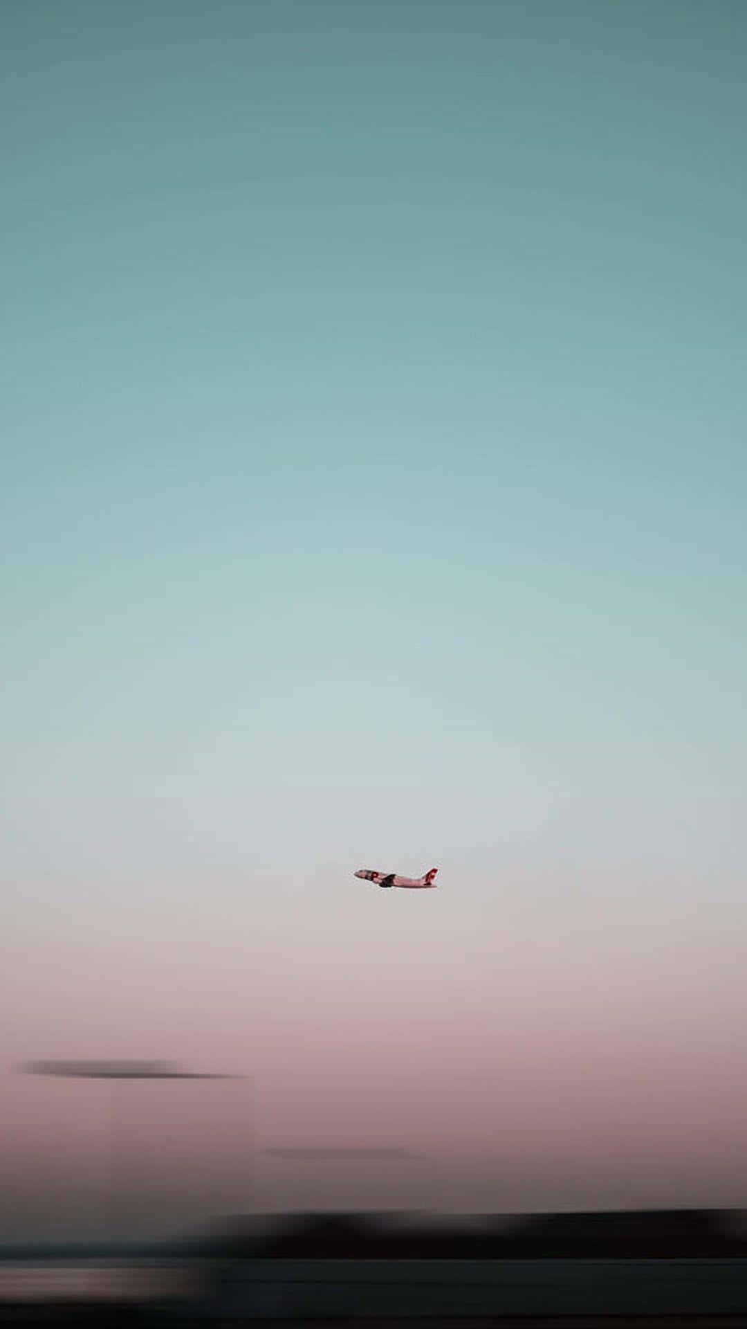 一架飛機在柔和的日落天空背景下飛行，下方是模糊的地面。
