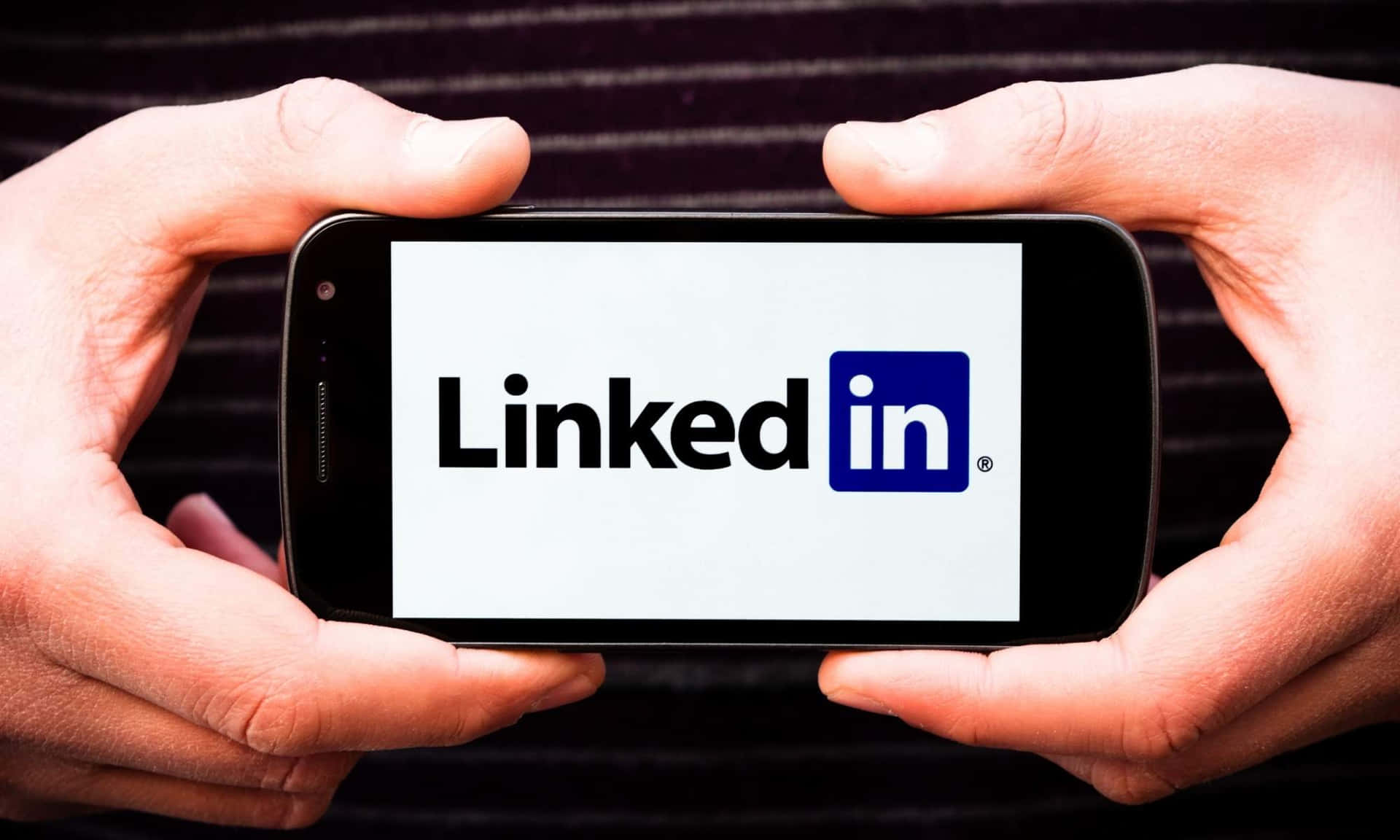 兩隻手拿著一部顯示LinkedIn標誌的智能手機。