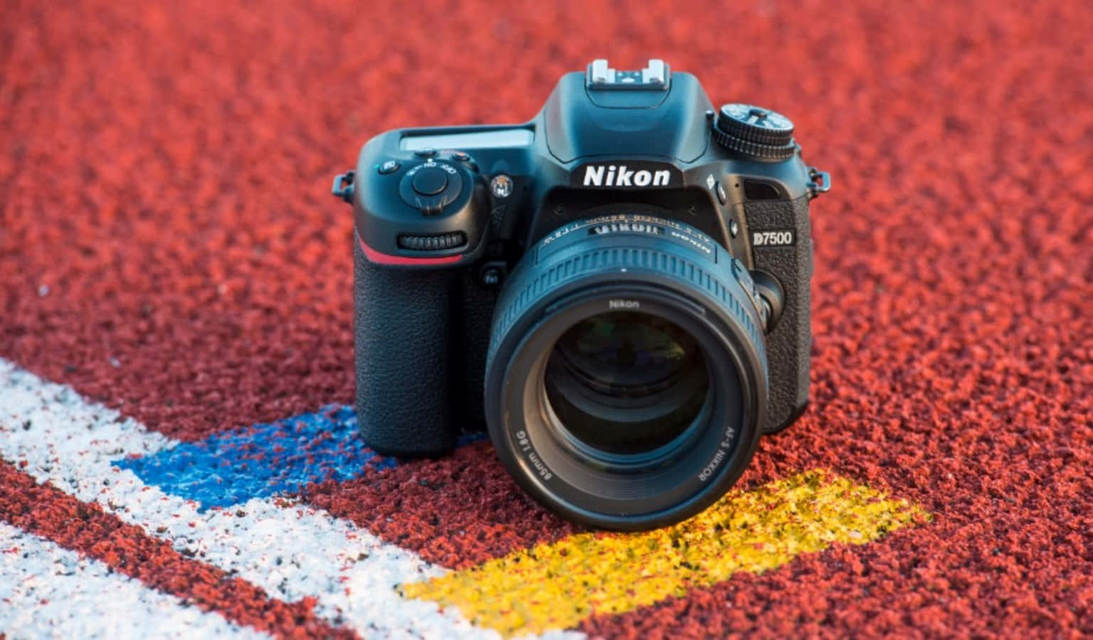 黑色 Nikon D7500 相機在紅色跑道上，帶有藍色和黃色標記。