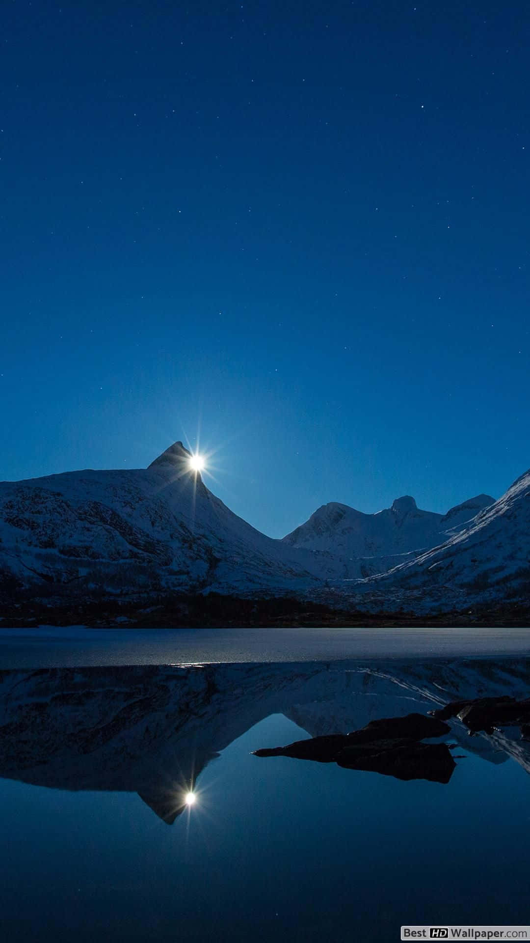 月光下白雪覆蓋的山峰倒映在夜間的冰凍湖面上。