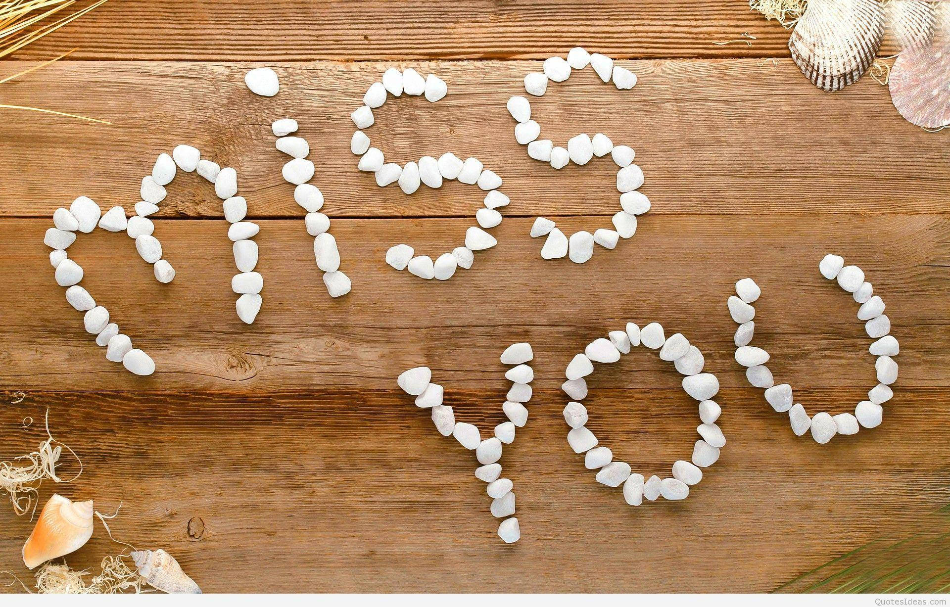 Love Quotes 桌布 壁紙 — 用白色鵝卵石拼出的「miss you」字樣，位於質樸的木質表面上，周圍環繞著貝殼和乾草。
