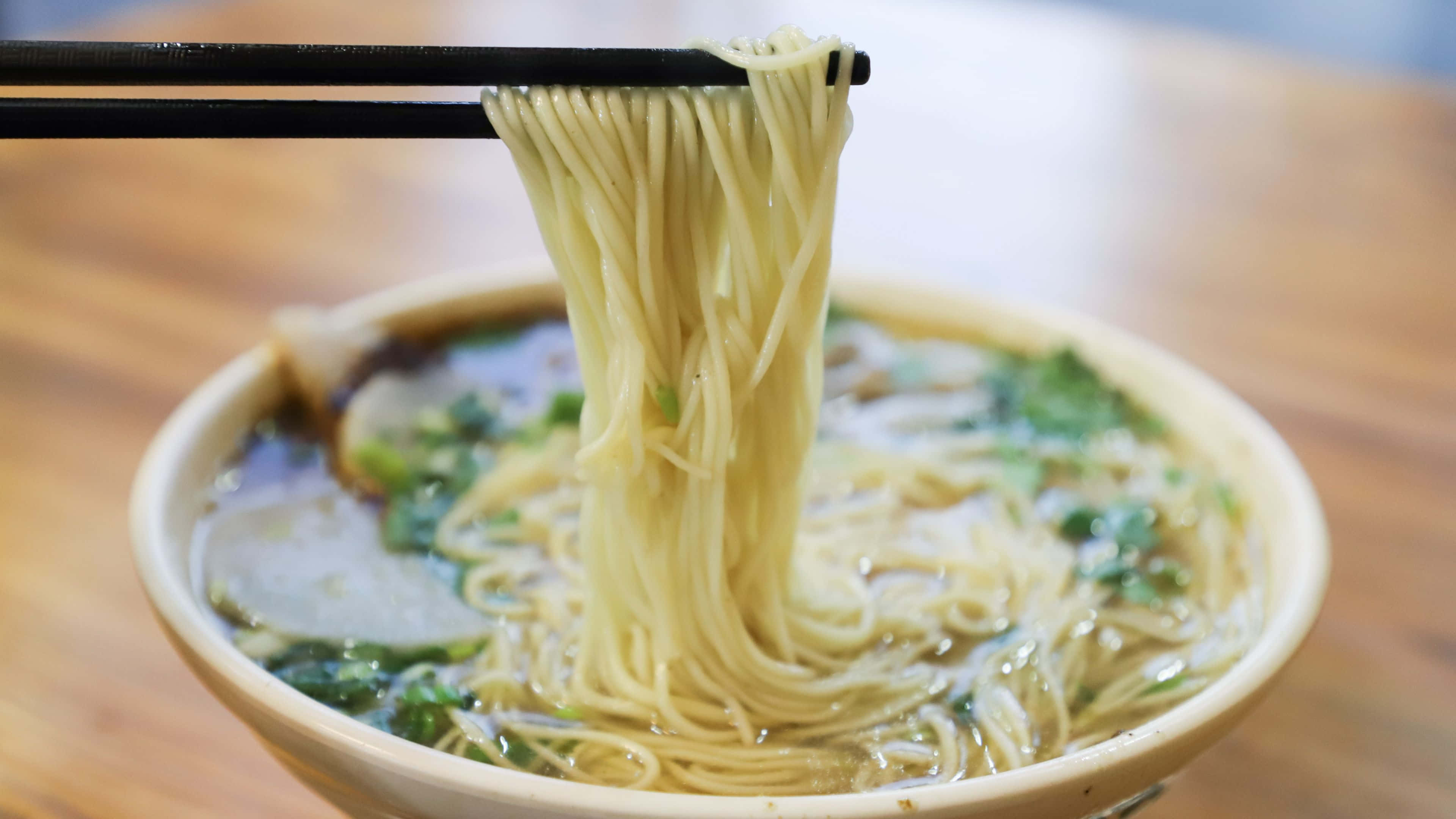 Noodles 桌布 壁紙 — 用筷子將麵條從湯中夾起的冒煙拉麵碗，配上蔥花和豬肉片。