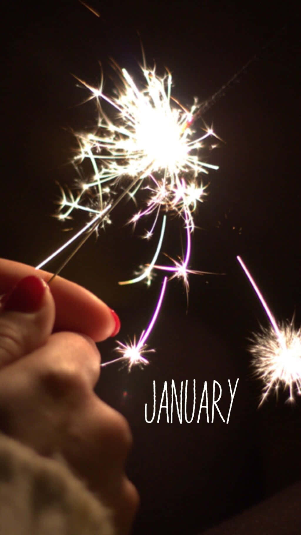 用這部電話為親愛的人送上新年祝福！ 壁紙 — 一隻塗有紅色指甲的手在漆黑的夜空中握著閃爍的煙花，下方寫有「january」一詞。
