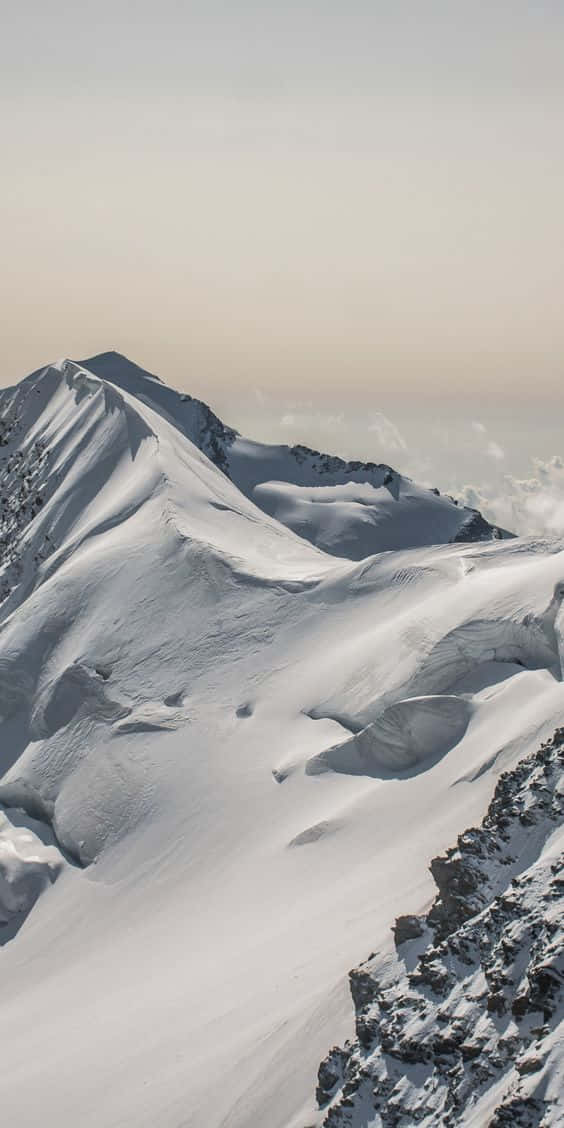 在蒼白天空下，帶有岩石露頭的雪山峰頂