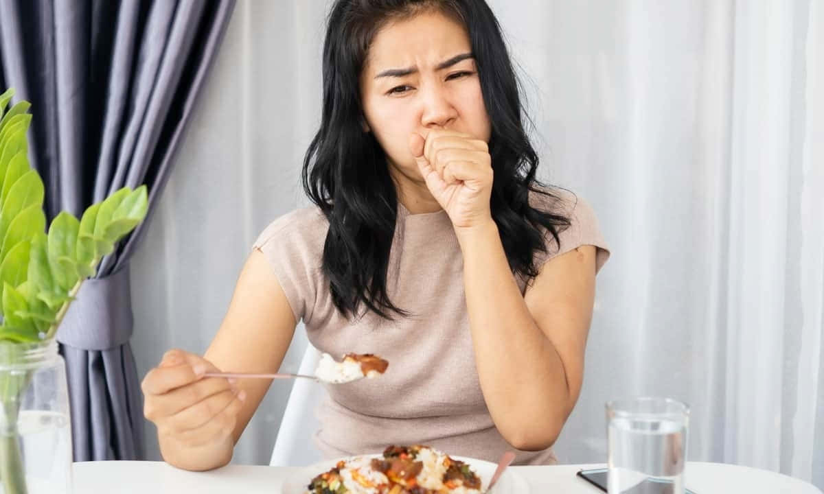 女士在餐桌前拿著一匙食物並捂住嘴巴。