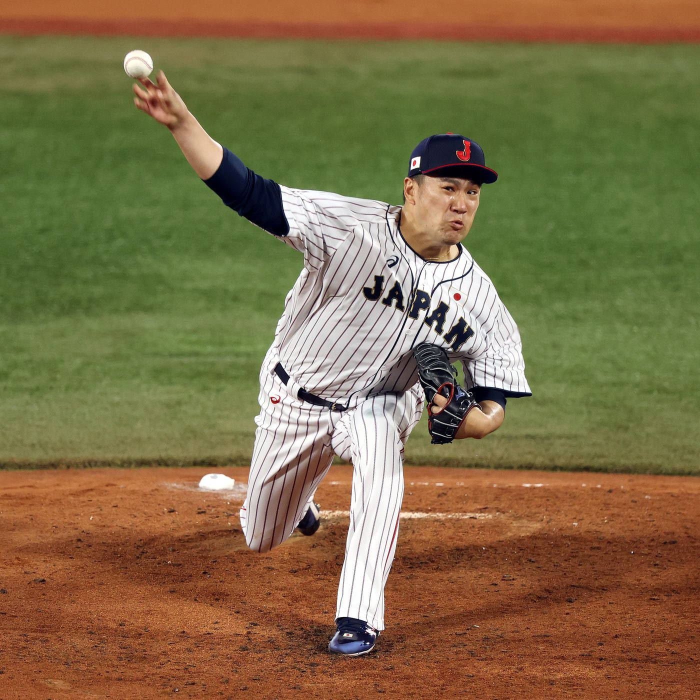 田中將大投出快速球 壁紙 — 一位身穿條紋球衣的日本棒球投手在夜間燈光明亮的球場上投球。