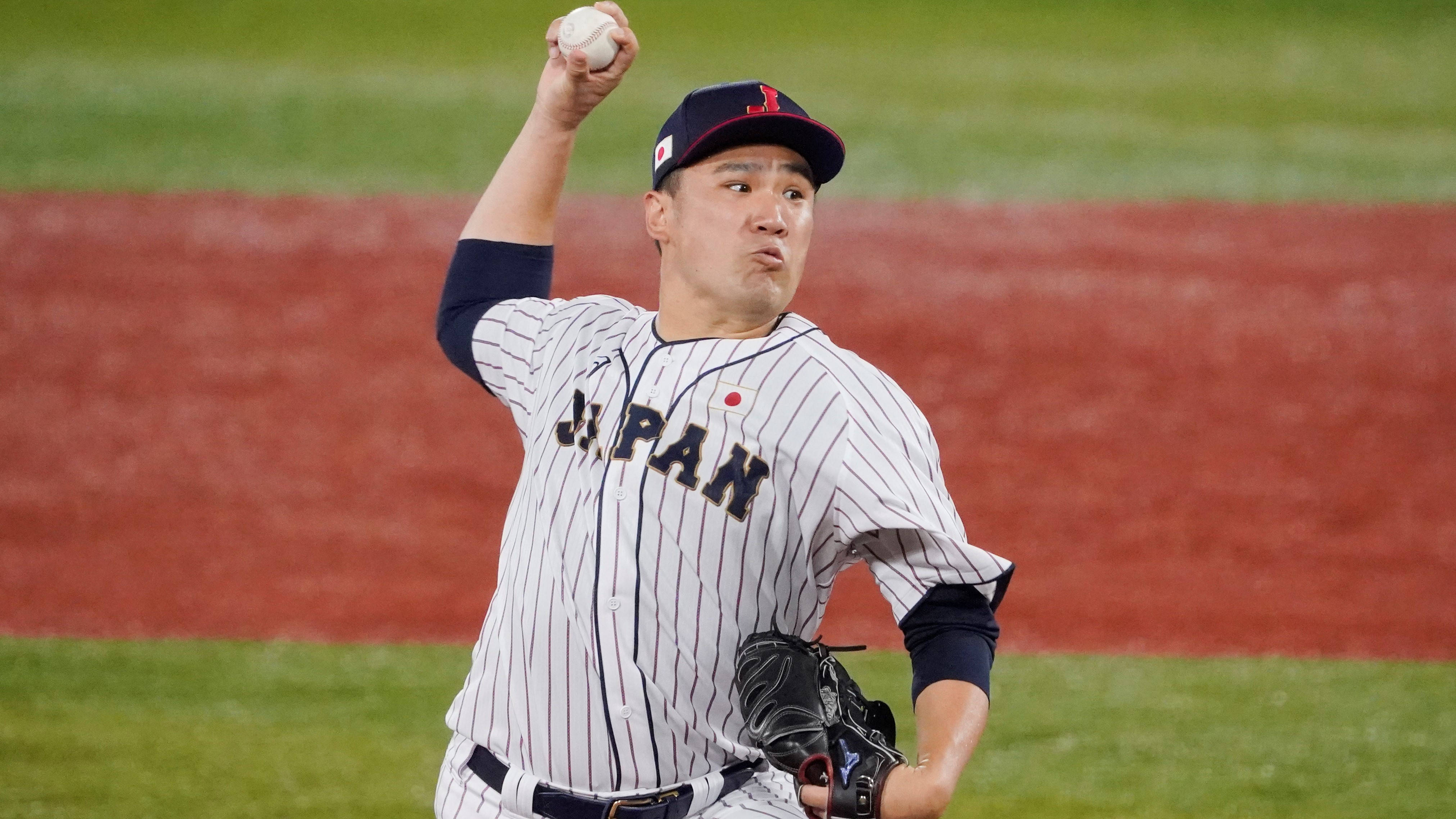 田中將大身穿日本隊球衣 壁紙 — 一位身穿條紋球衣的日本棒球投手在夜間光線充足的球場上準備投球。