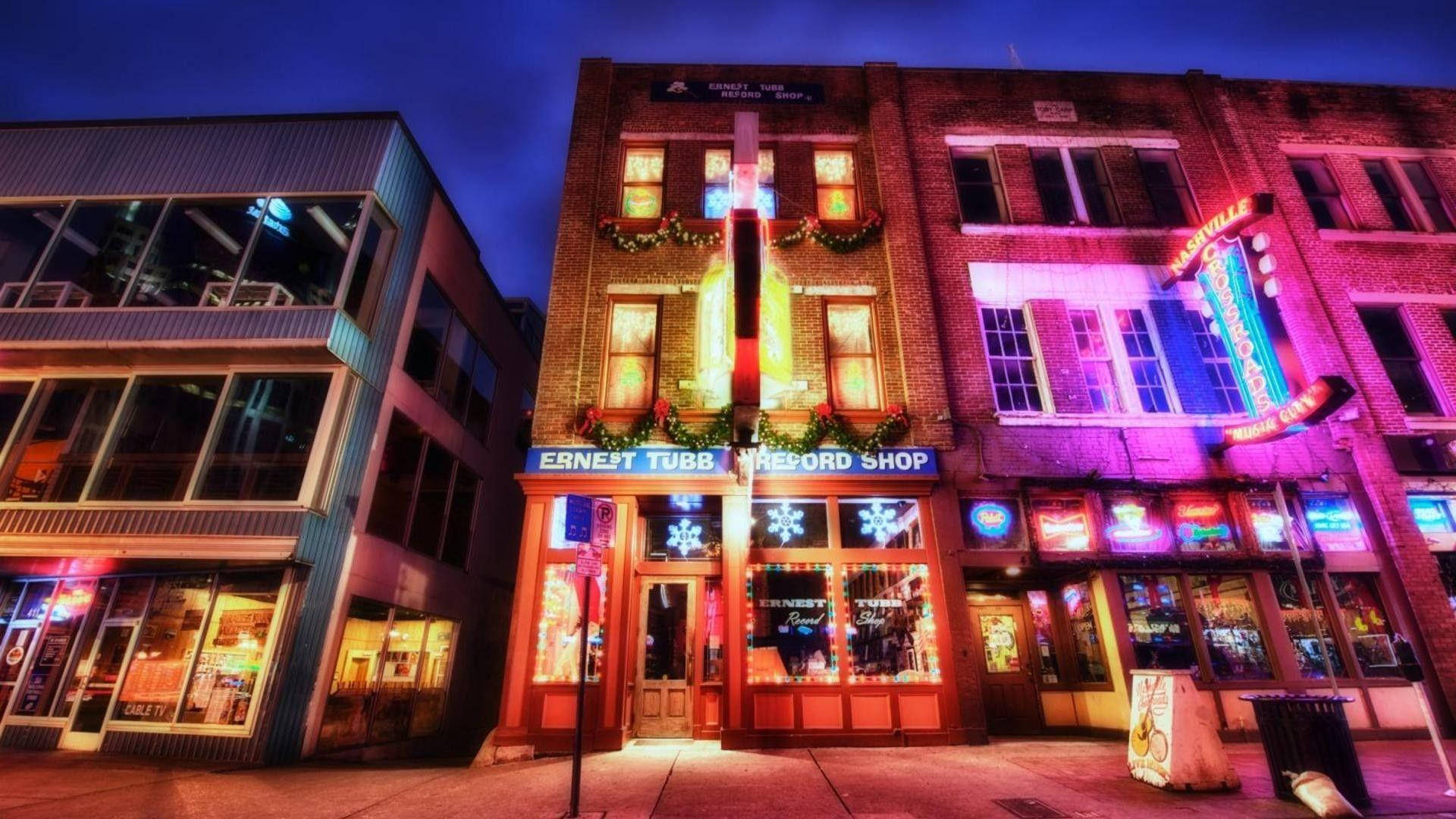 田納西州納什維爾夜間街景商店 壁紙 — 充滿活力的霓虹燈照亮了夜晚的節日城市街道，節日裝飾點綴著磚砌建築。