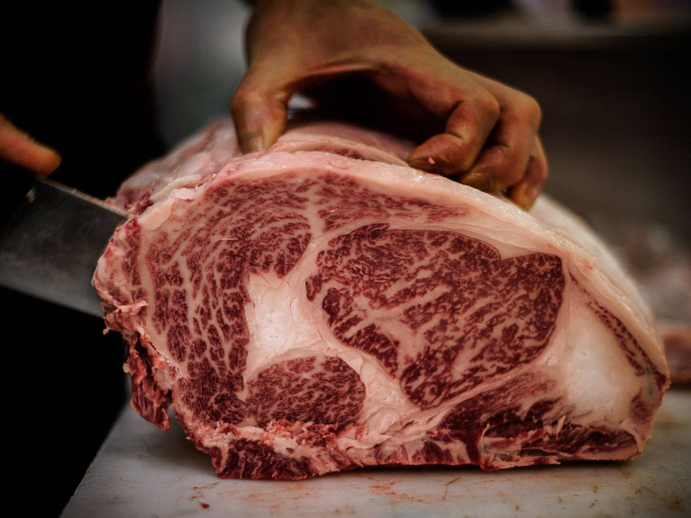 手用刀喺砧板上切開大理石紋牛肉。