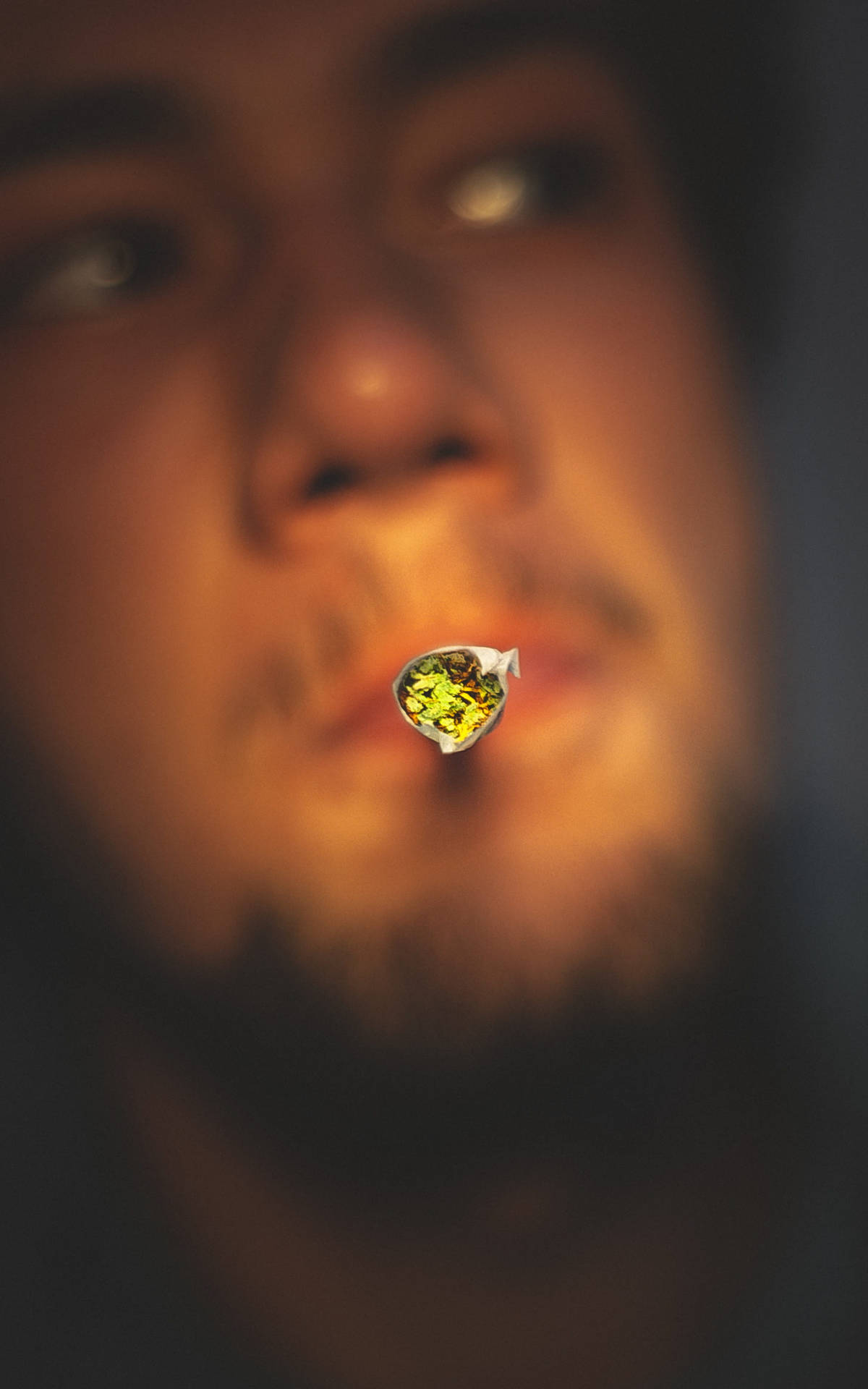 一個人在溫暖的燈光下拿著一根點燃的大麻煙，臉部模糊。