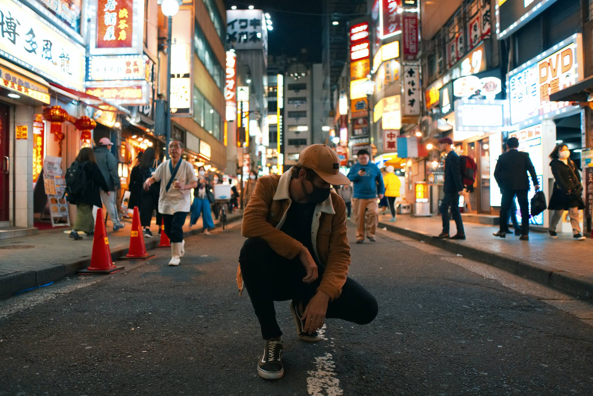 在夜晚繁忙的東京街道上，在發光的霓虹招牌下蹲下的人。