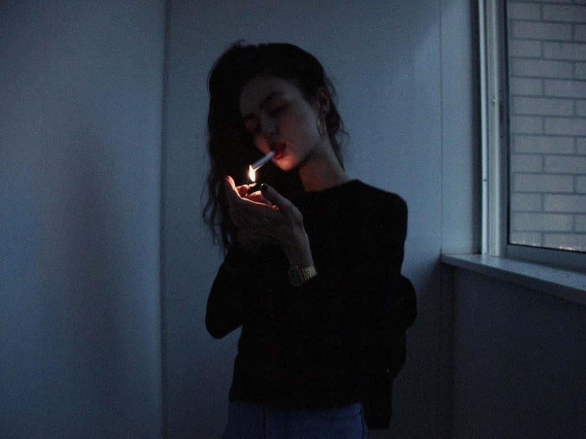 女人在昏暗的藍光下，在室內窗邊點燃香煙。