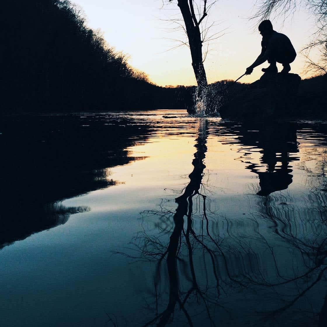 一個人在日落時分從岩石上向平靜的湖面潑水。