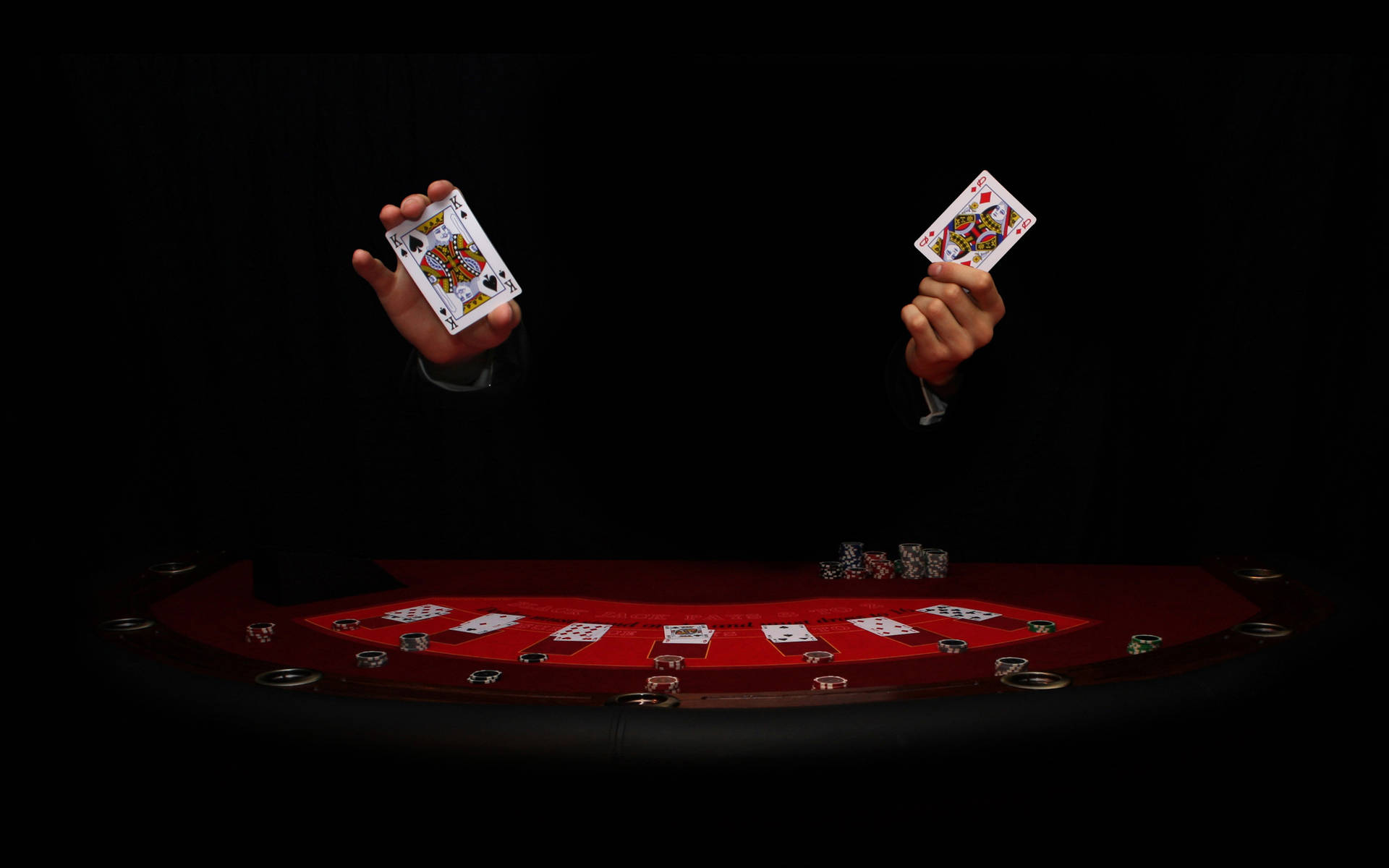 兩隻手在帶有籌碼的紅色遊戲桌上高舉撲克牌。