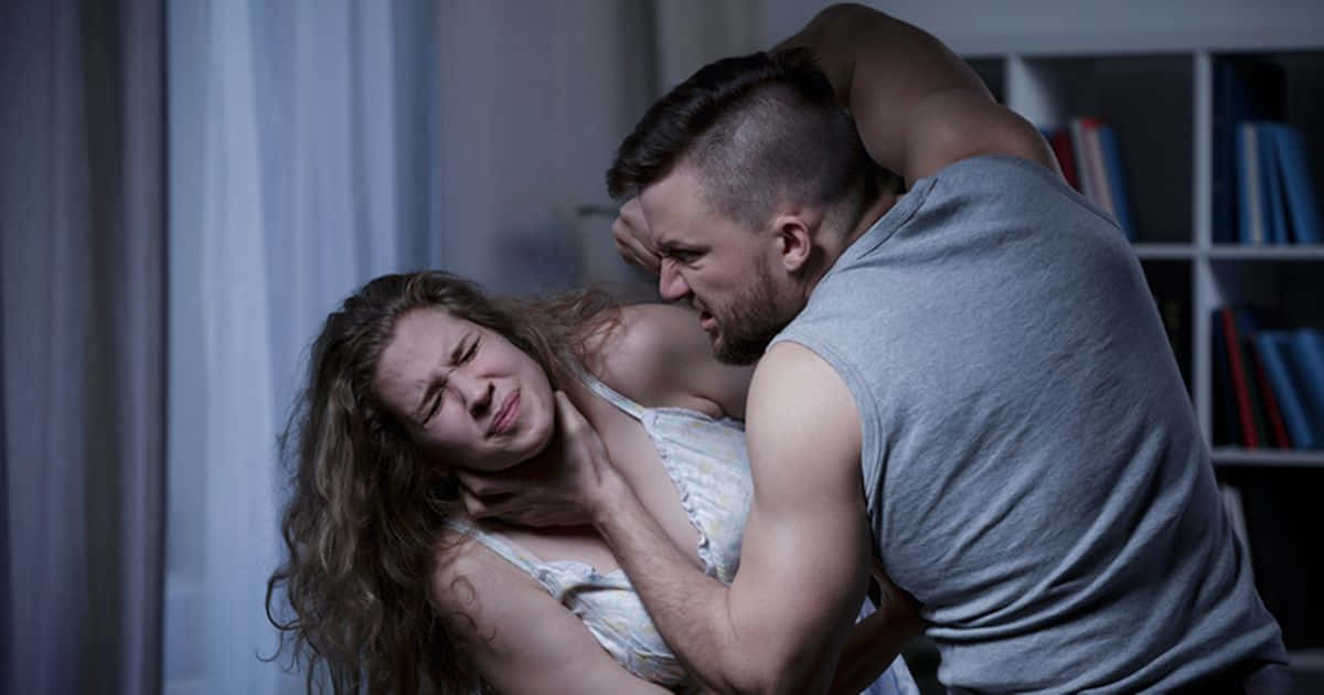 一名男子在光線昏暗的房間內掐住一名女子的脖子，背景有書架。