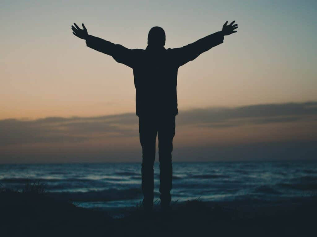 日落時分在沙灘上張開雙臂的人的剪影。