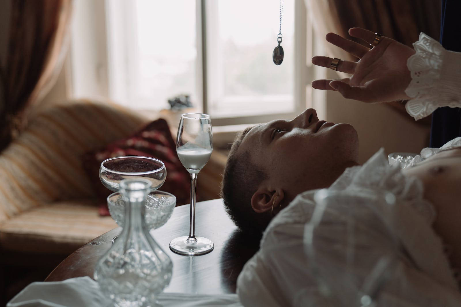 男子旁有眼鏡接受催眠 壁紙 — 一個人躺在桌子上，另一隻手在懸掛的吊墜和水晶杯附近盤旋在他們上方。