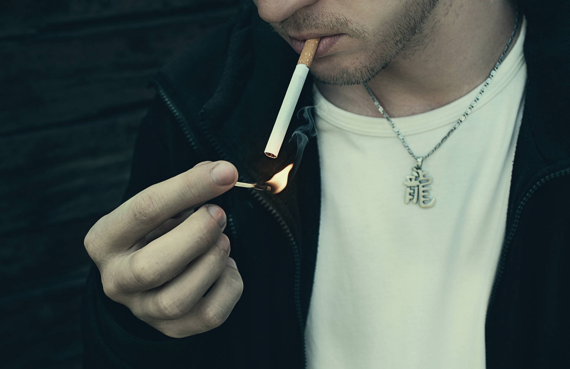 男子用火柴點煙，佩戴龍形吊墜項鍊。