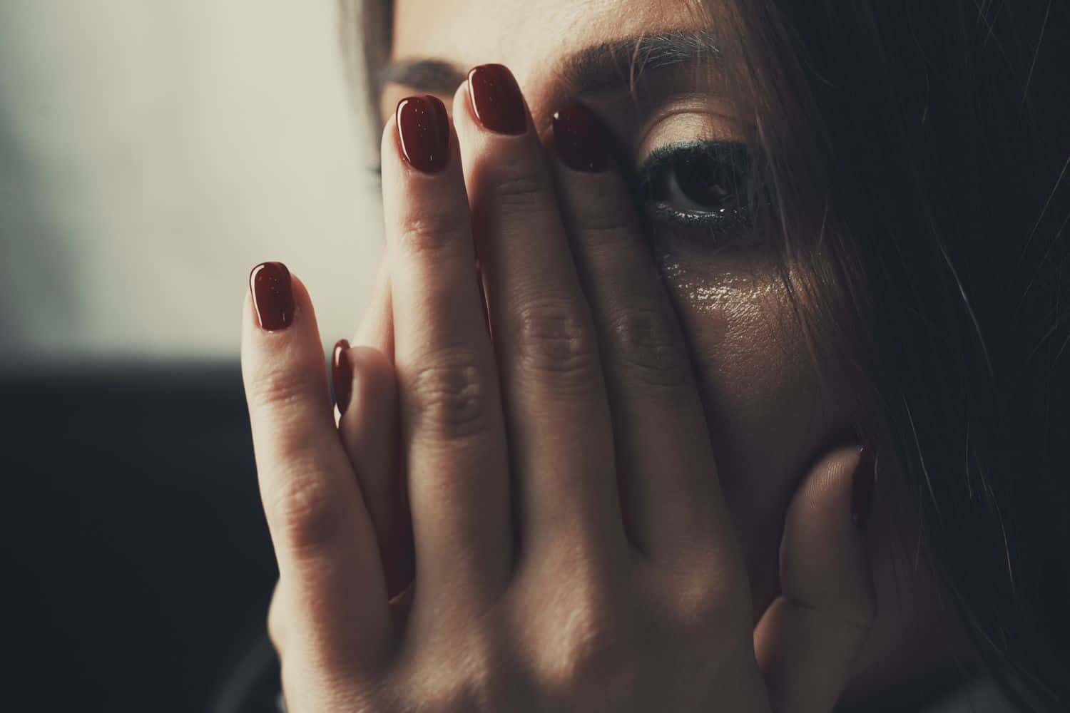 男子痛哭 壁紙 — 一個紅指甲女人用一隻手遮住臉，在昏暗的特寫中露出一隻含淚的眼睛。