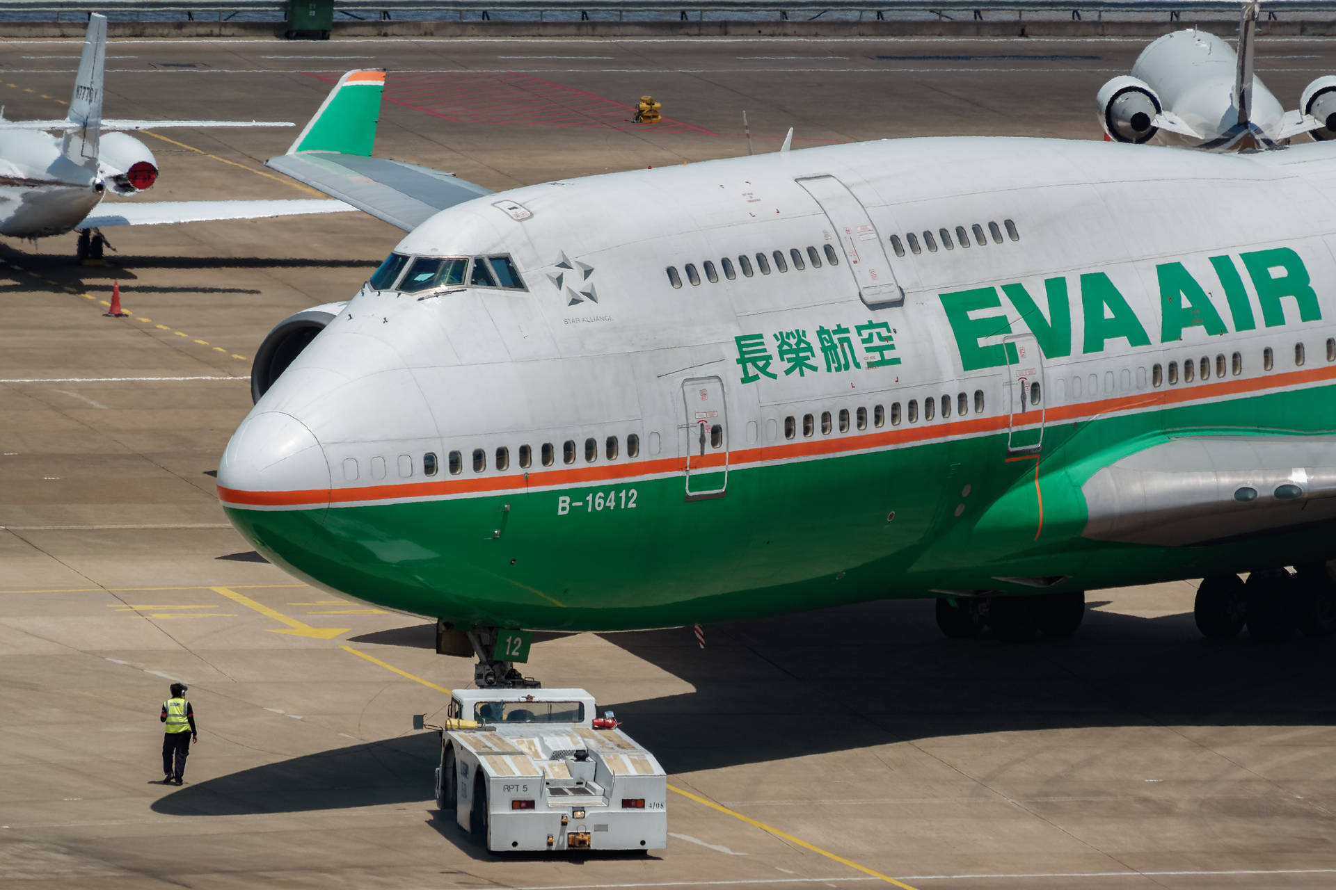 長榮航空珍寶客機停泊在機場停機坪，有地勤人員和牽引車。