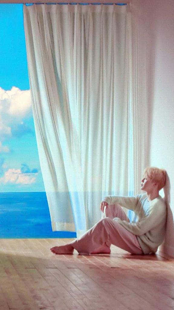 赤腳坐在木地板上，望向窗外的海洋和天空的人。
