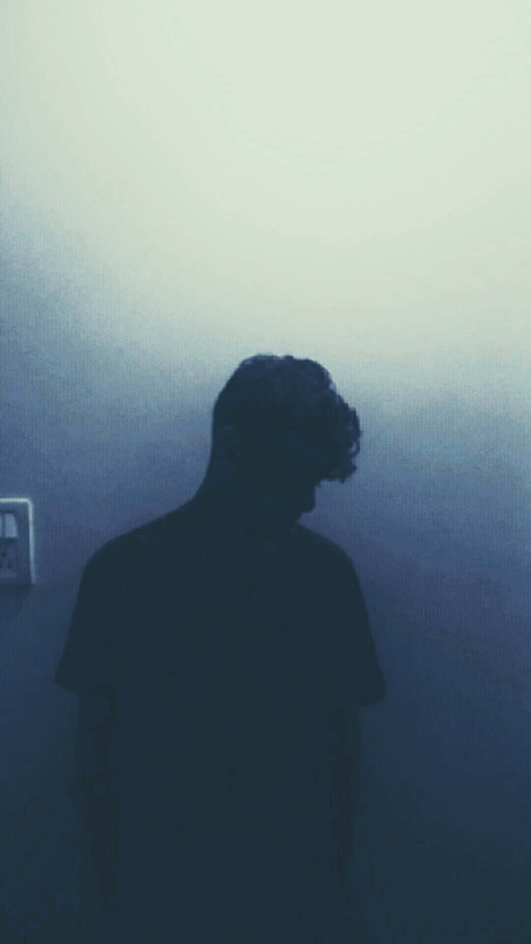 一個人的剪影獨自站在昏暗的藍色房間裡，低著頭。