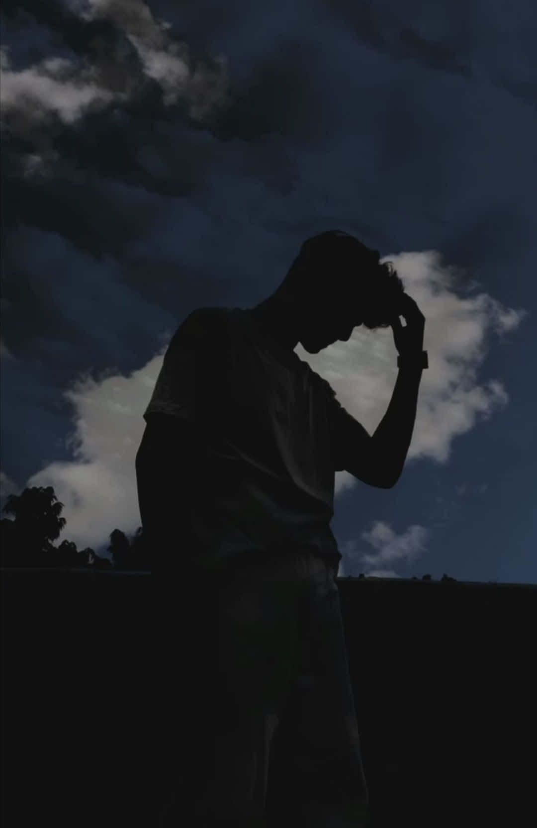 一個人的剪影，在黑暗的多雲天空下抱著頭。