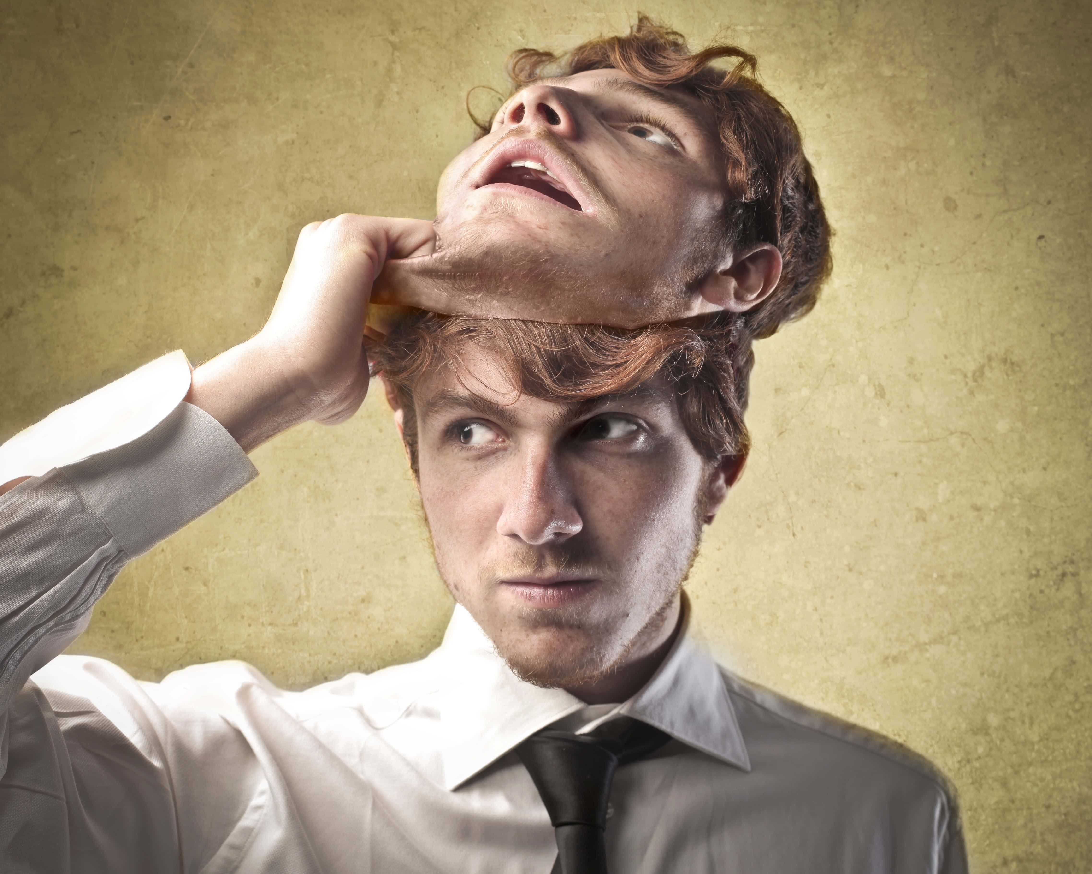 男性摘下與臉部相同的面具 壁紙 — 一個穿著襯衫打領帶的男人，在質感米色牆壁上，抓住自己斷頭的脖子。