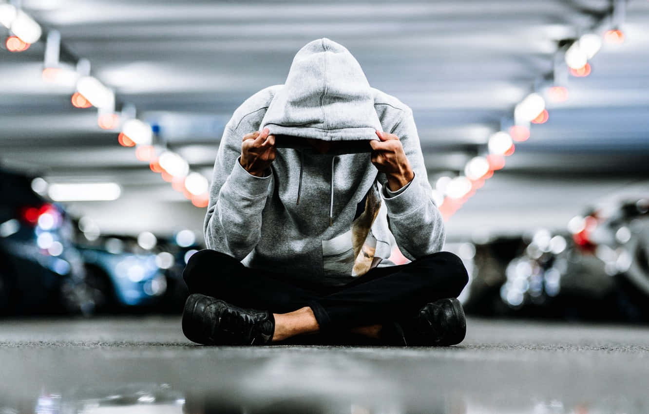 男性經理在辦公 壁紙 — 一個穿著灰色連帽衫的人盤腿坐在停車場地板上，雙手抱頭。