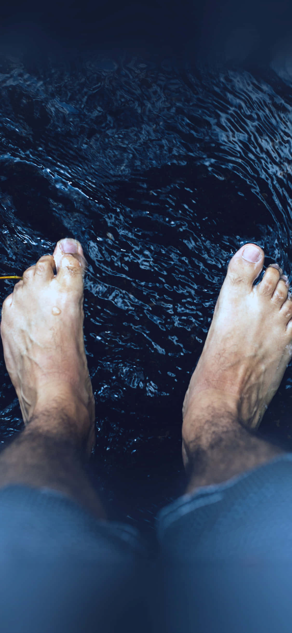 男性腳部浸在溪流中 壁紙 — 一個人的赤腳站在深暗的水中，周圍有漣漪旋轉。