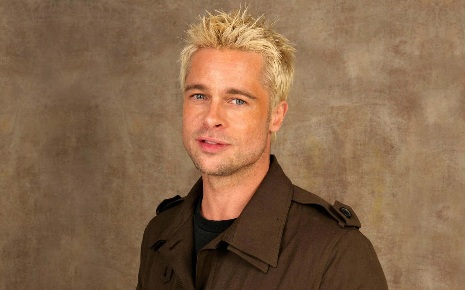 Brad Pitt 桌布 壁紙 — 畢彼特（Brad Pitt）留著尖刺金髮和藍眼睛，身穿棕色風衣，背景為有紋理的米色背景。