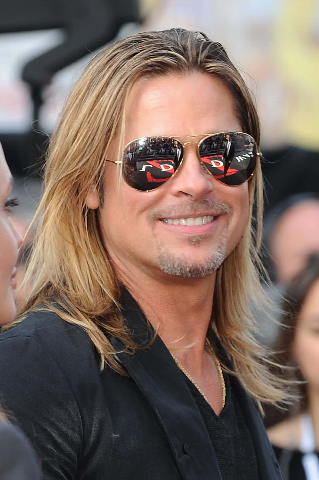 Brad Pitt 桌布 壁紙 — 畢彼特自信地微笑，戴著飛行員太陽眼鏡，在公開活動中，背景人物模糊。