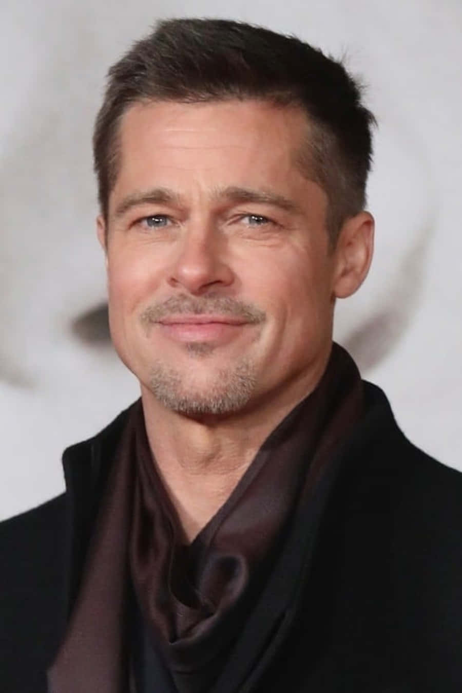 Brad Pitt 桌布 壁紙 — 畢彼特身穿黑色西裝，搭配深棕色緞面圍巾，在柔和模糊的背景前溫暖微笑。