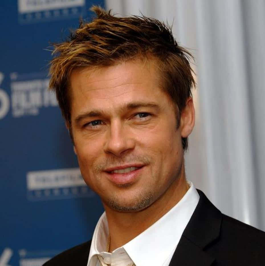 Brad Pitt 桌布 壁紙 — 畢彼特身穿黑色西裝和白色襯衫，在藍色活動背景前溫暖地微笑。
