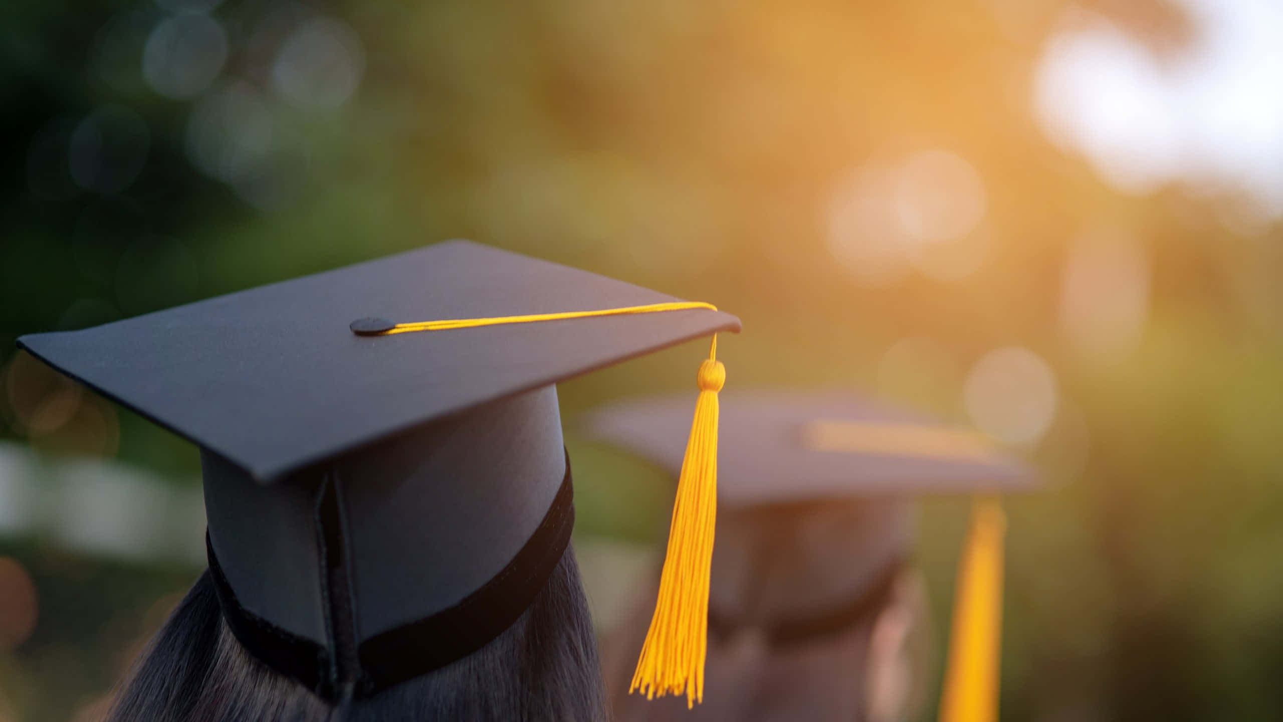 Graduation Ceremony 桌布 壁紙 — 畢業帽特寫，帶有亮黃色流蘇，背景是溫暖的金色日落。