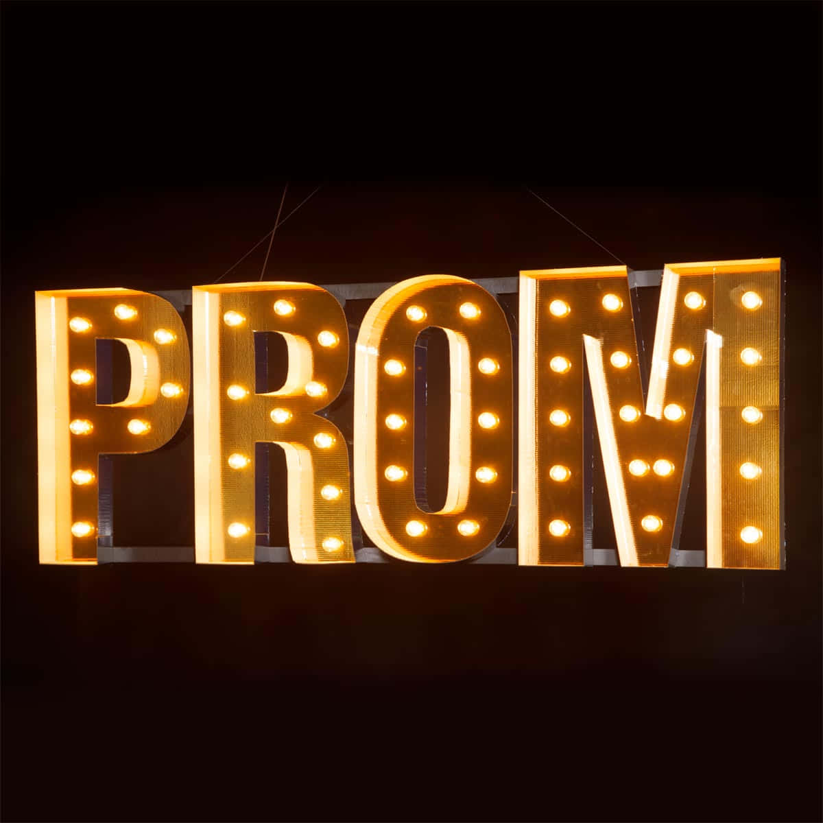 發光的帳篷標誌拼出PROM，帶有溫暖燈光，背景為深色。