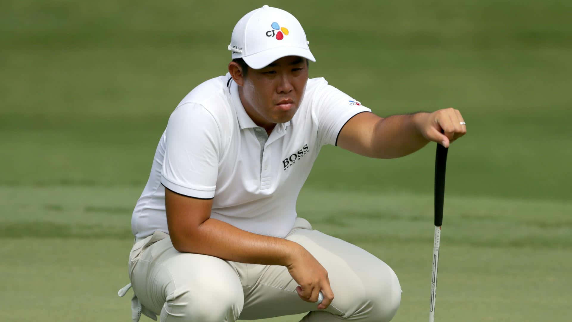 畢永勳全神貫注 壁紙 — 一位身穿白色衣服、專注的高爾夫球手在綠色高爾夫球場上蹲下，手持推桿。